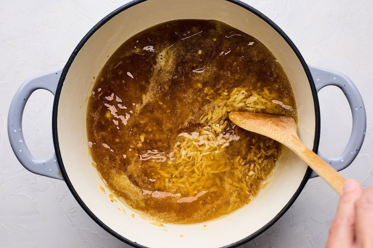 stirring broth into orzo in pot with wooden spoon.