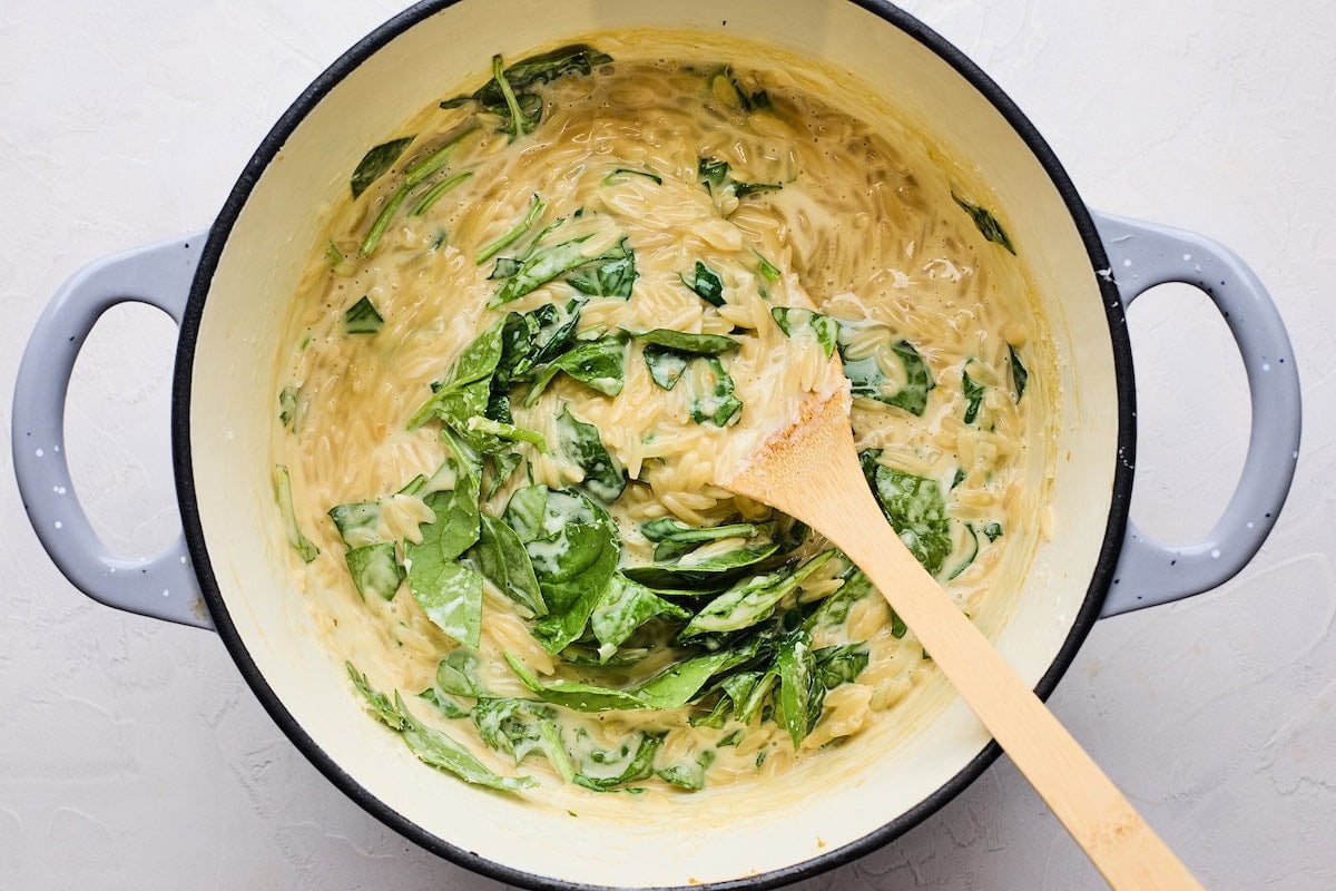 creamy orzo with spinach in pot with wooden spoon.