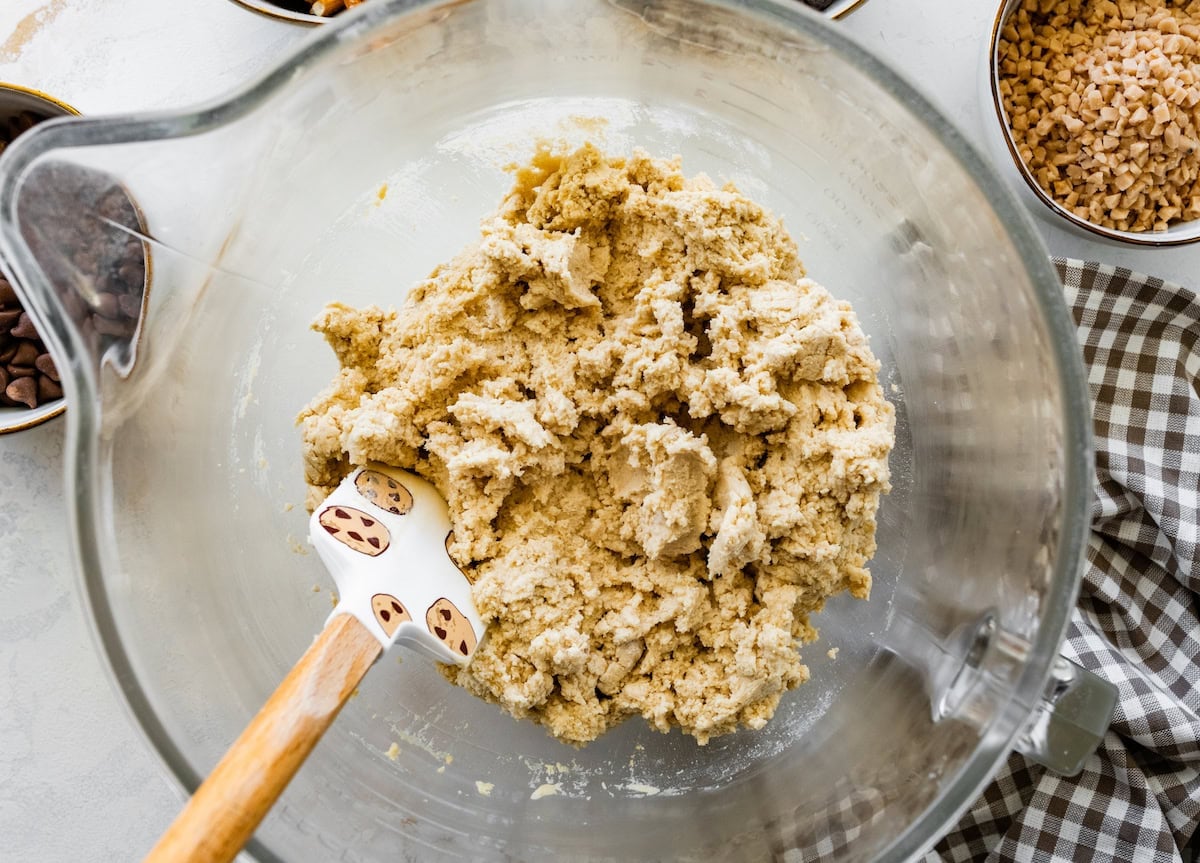 cookie dough being mixed together with spatula in mixing bowl.