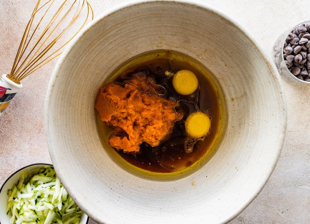 pumpkin, oil, maple syrup, eggs, and vanilla in mixing bowl to make pumpkin zucchini muffins.