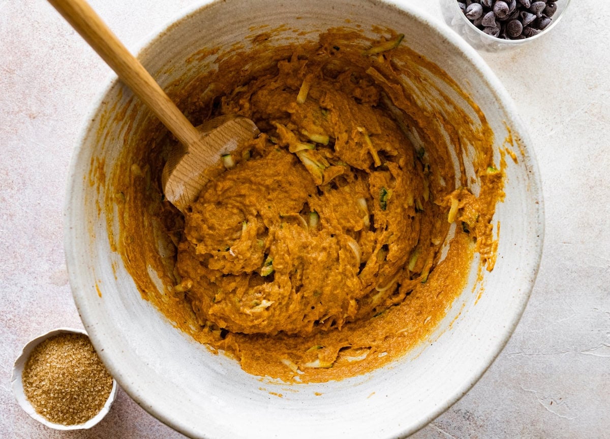 pumpkin zucchini batter in mixing bowl with wooden spoon.
