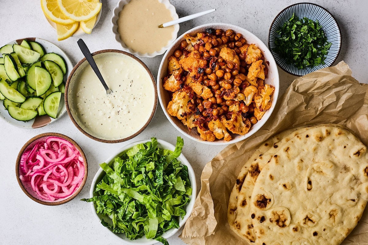 roasted cauliflower chickpeas, naan bread, lettuce, pickled red onions, cucumbers, feta yogurt spread, tahini dressing, and herbs to make wraps.