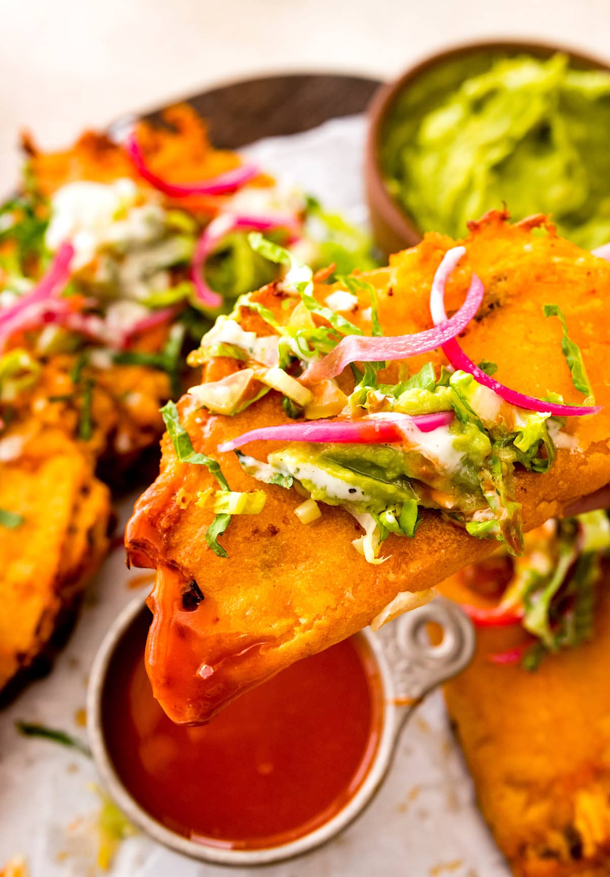 crispy buffalo chicken taco being dunked in buffalo sauce.