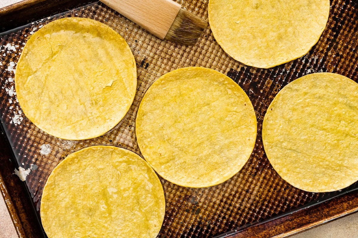 corn tortillas being brushed with oil on baking sheet to make crispy buffalo chicken tacos.