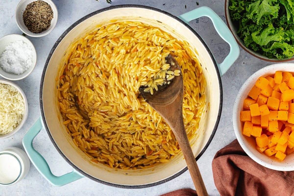 cooking butternut squash orzo in pot with wooden spoon.