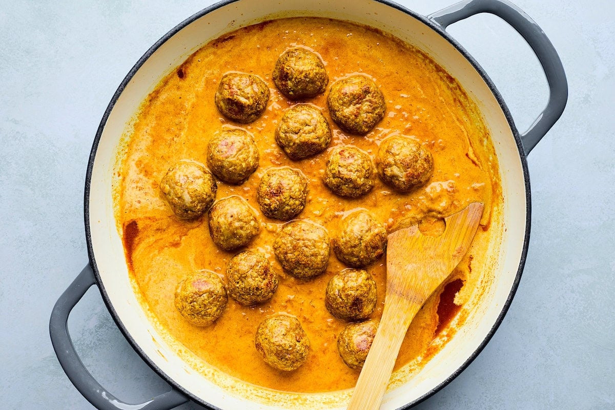 tikka masala meatballs in pot with sauce and wooden spoon.