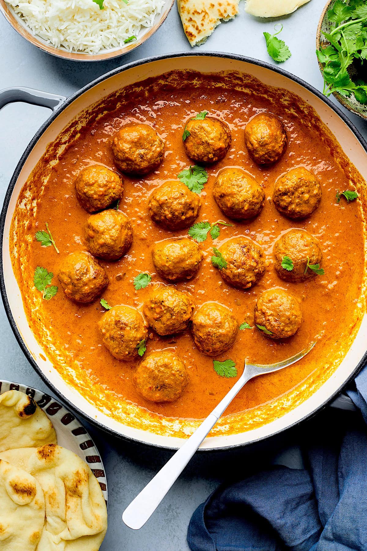 tikka masala meatballs in sauce in pot with cilantro and spoon.