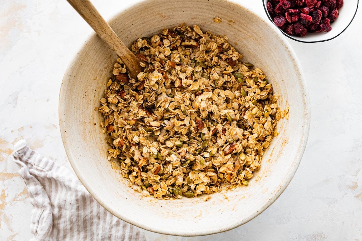 granola ingredients in mixing bowl with wooden spoon.
