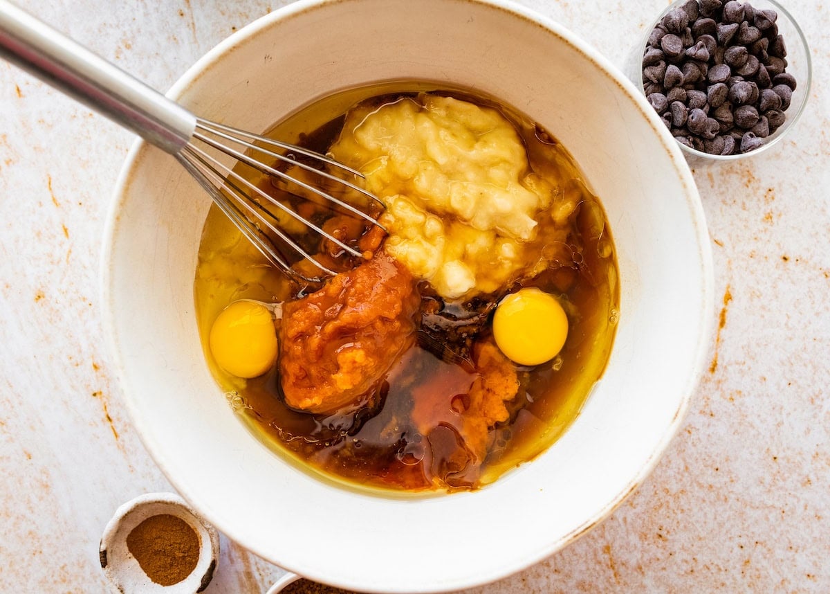 banana, pumpkin, sugar, oil, and eggs in mixing bowl with whisk.