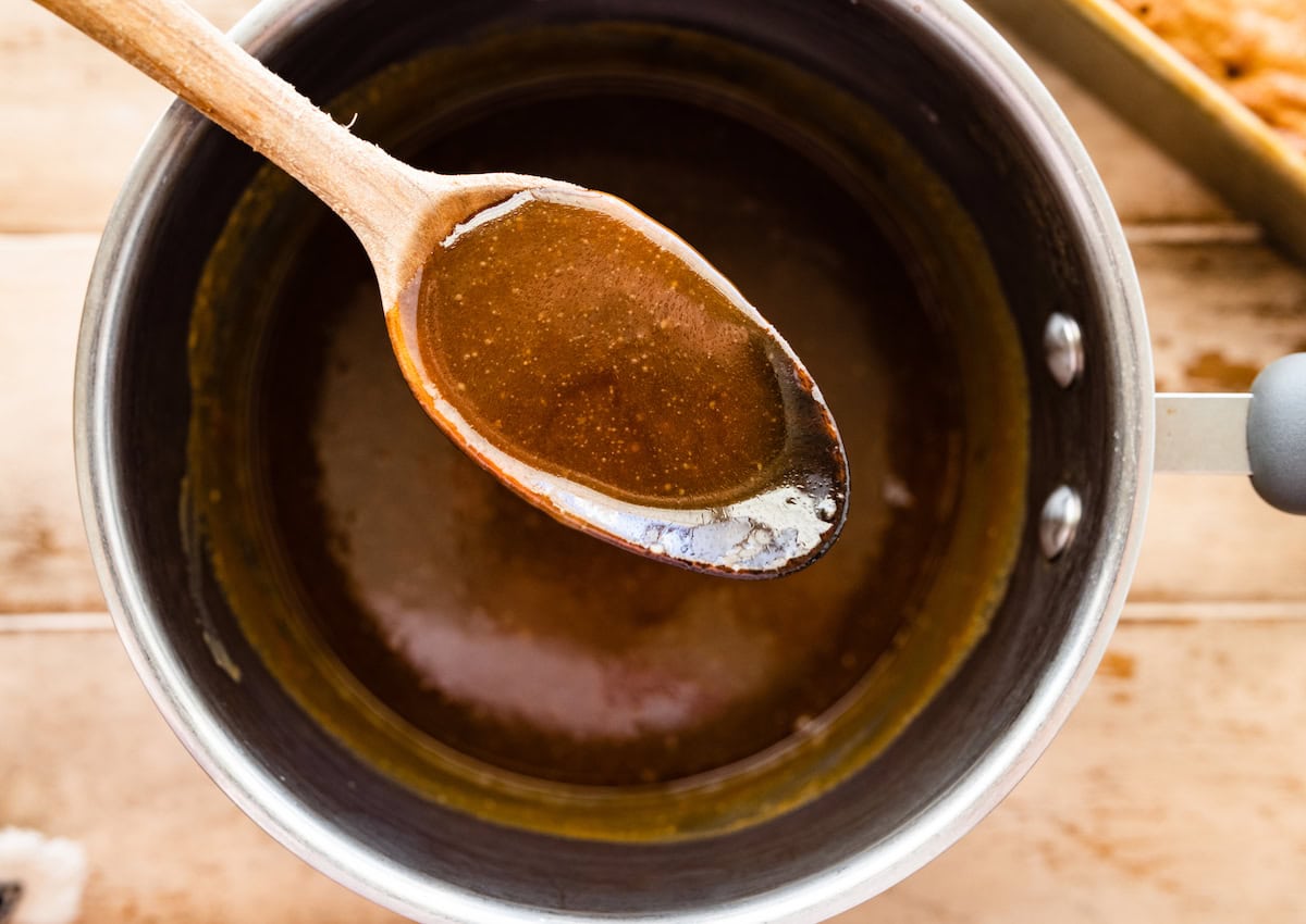 toffee sauce in spoon over saucepan of toffee sauce.