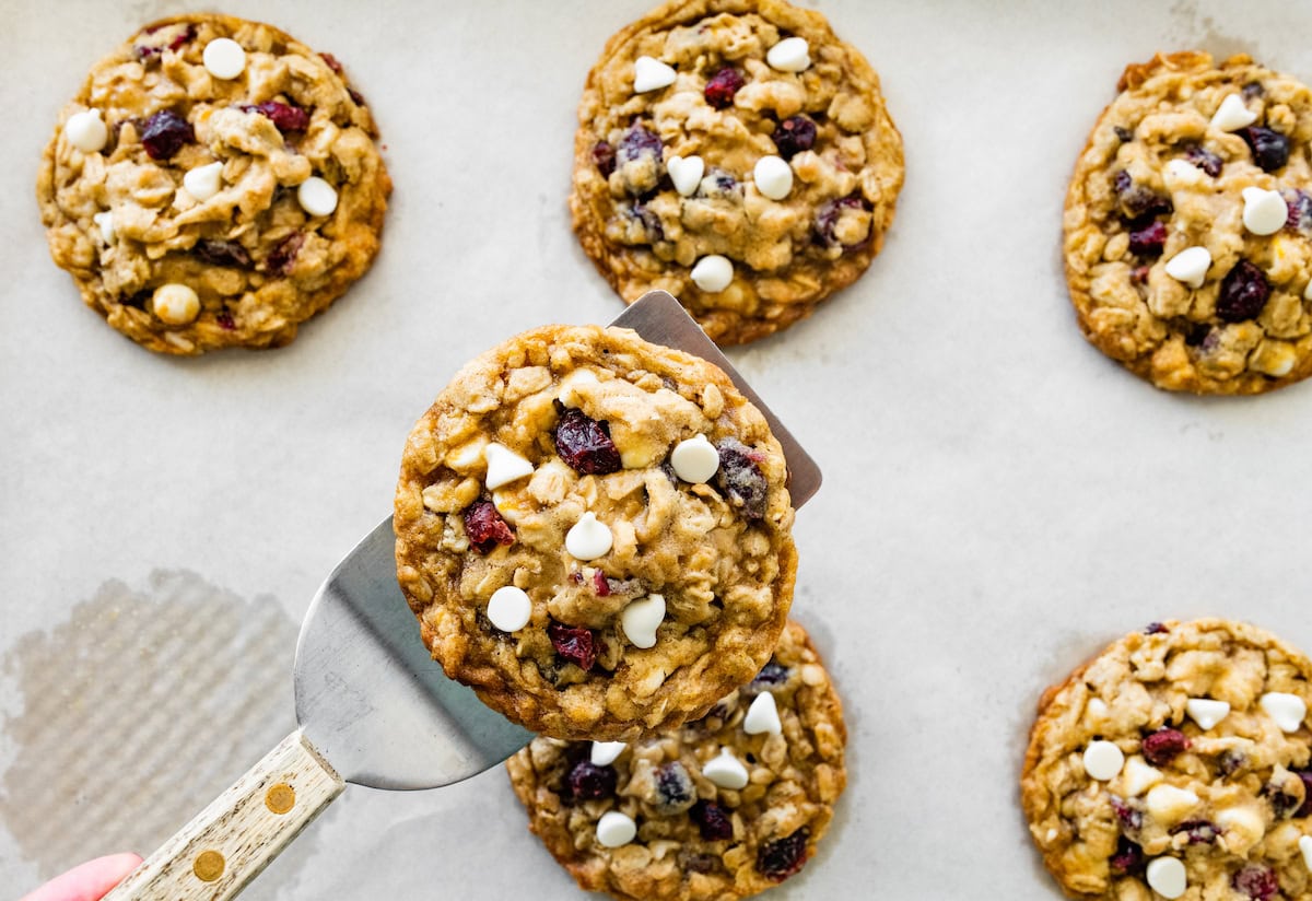 cranberry orange white chocolate oatmeal cookie being lifted off the baking sheet with a spatula.