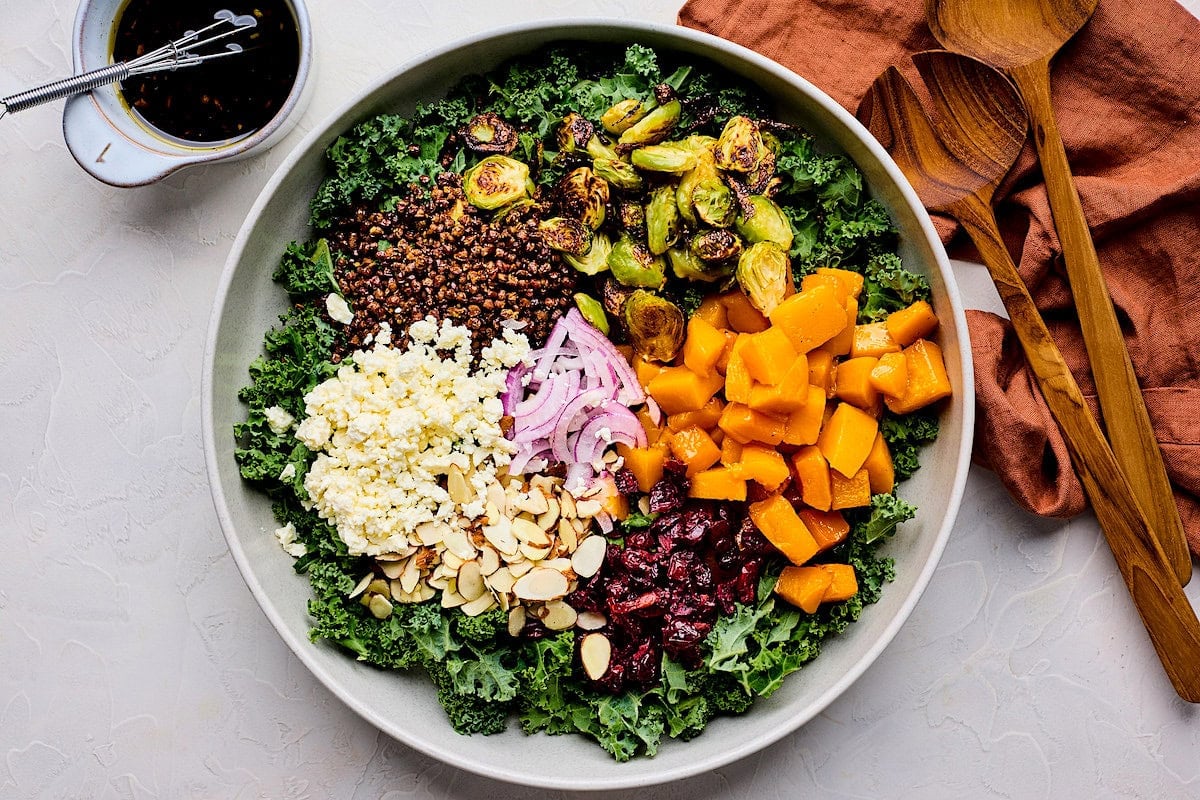 kale, butternut squash, brussels sprouts, lentils, feta, almonds, dried cranberries, and red onion in serving bowl.