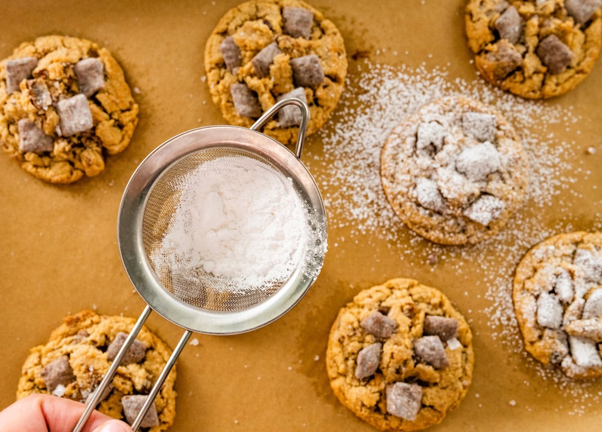 confectioner's sugar being sifted over puppy chow cookies.