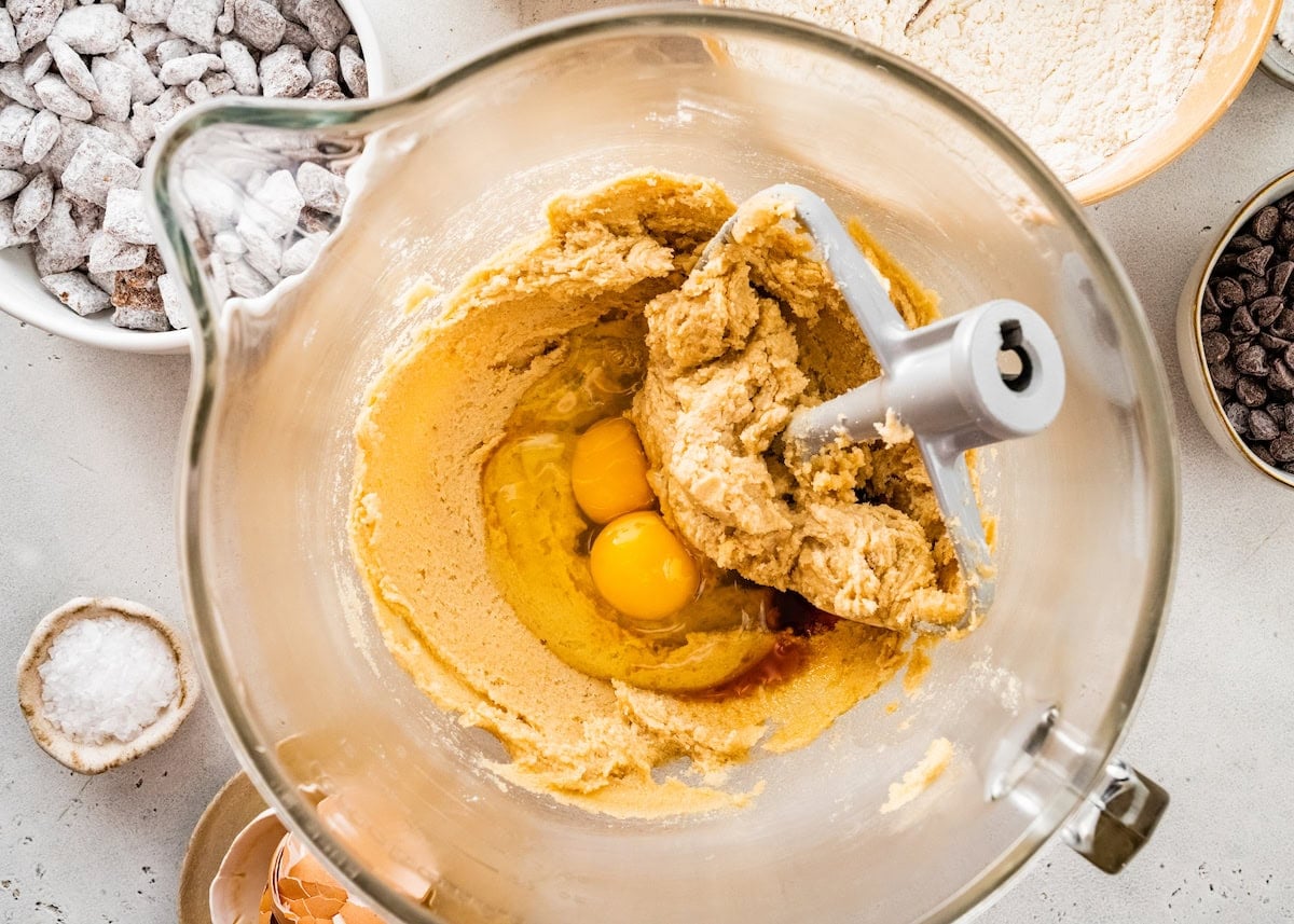 butter, peanut butter, and sugars being mixed in mixing bowl with eggs being added.