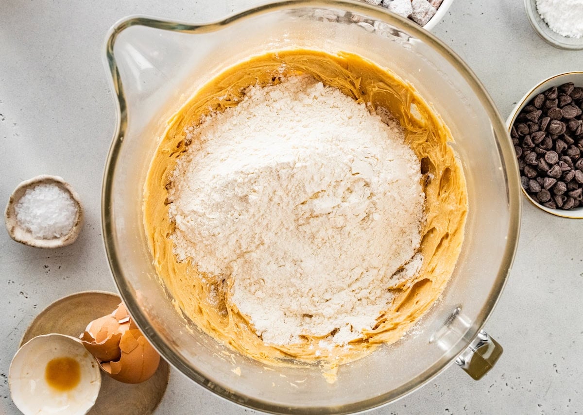 dry ingredients being added to puppy chow cookie dough in mixing bowl.