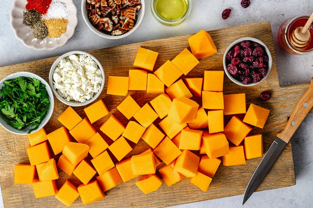 butternut squash cut into cubes on cutting board with knife.