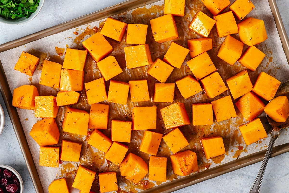 butternut squash cubes tossed in hot honey dressing on baking sheet with parchment paper.