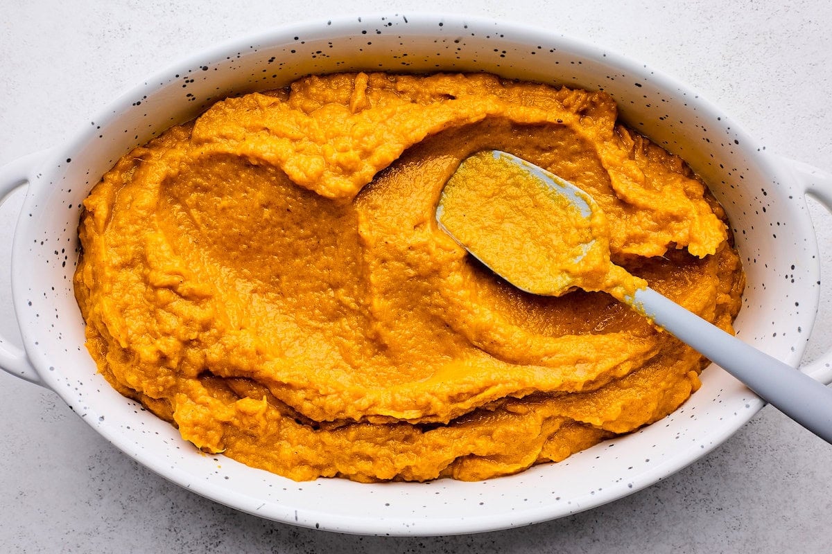 sweet potato casserole filling being spread in baking dish with spatula.