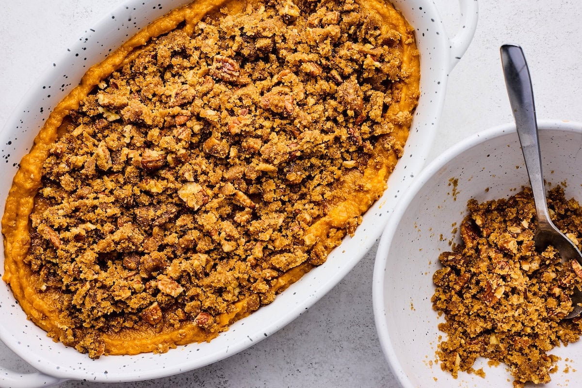 brown sugar pecan topping being sprinkled on top of sweet potato casserole in baking dish.