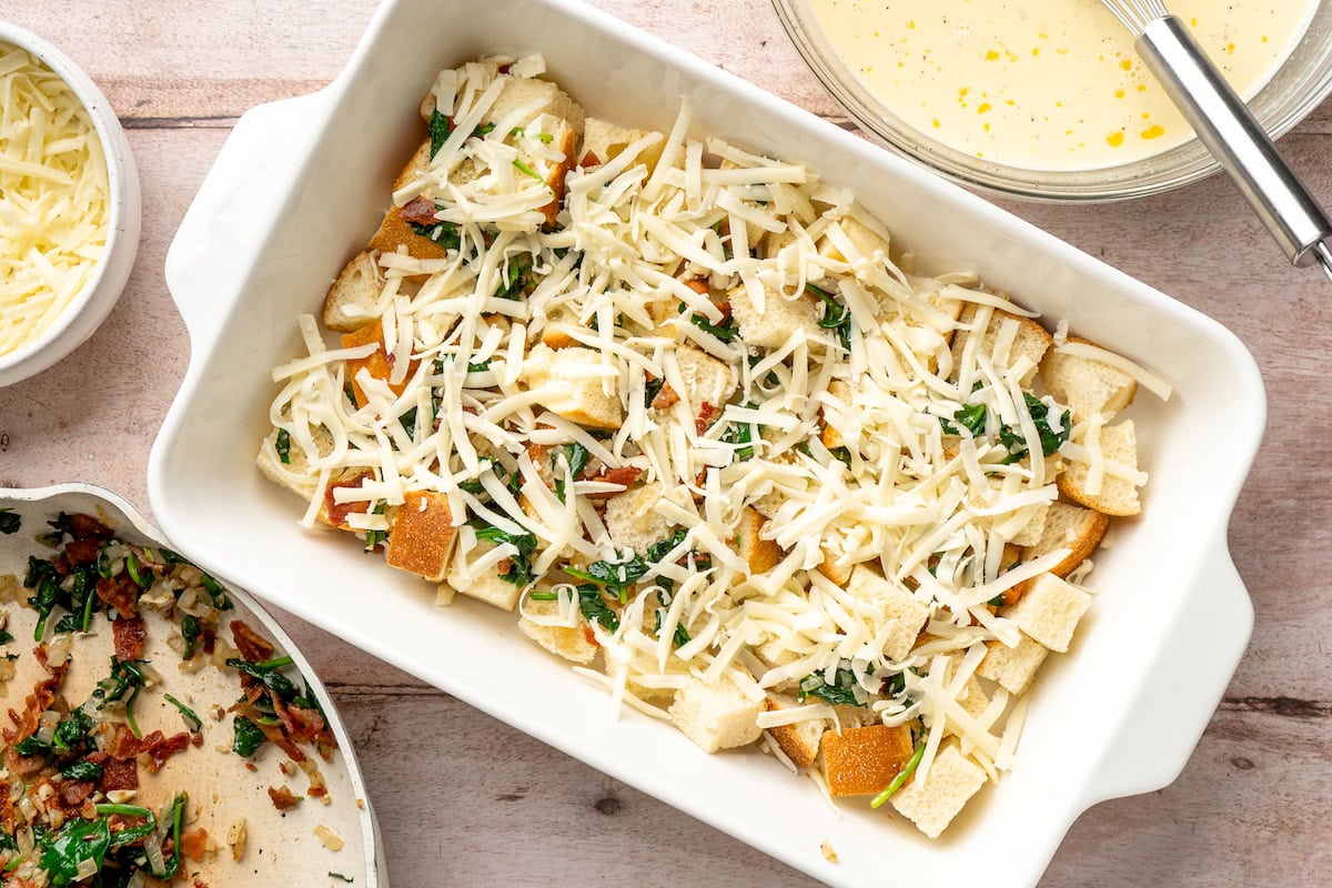 bread cubes, spinach, bacon, and shredded cheese in baking dish to make breakfast strata.