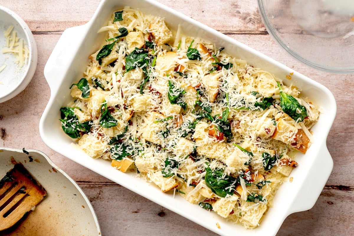 spinach bacon breakfast strata topped with cheese in baking dish ready to be chilled.