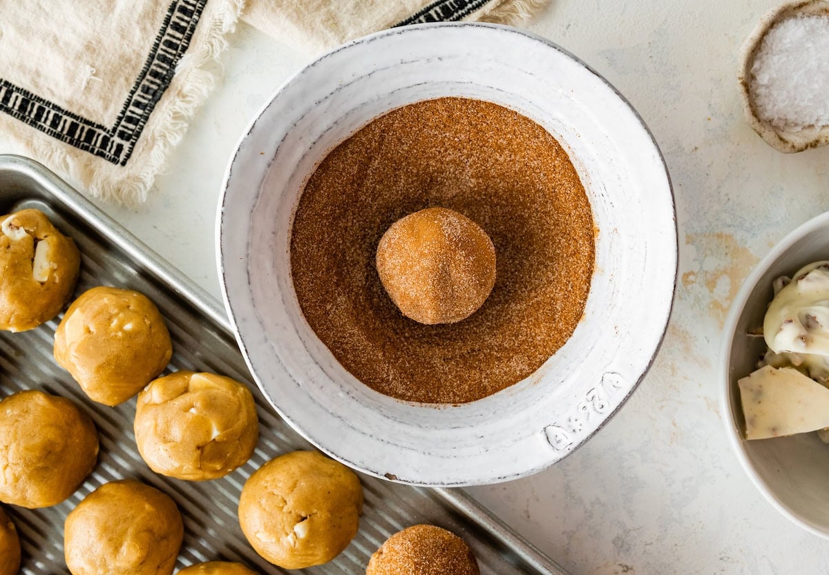 brown butter white chocolate candied pecan cookie dough ball being rolled in cinnamon and sugar.