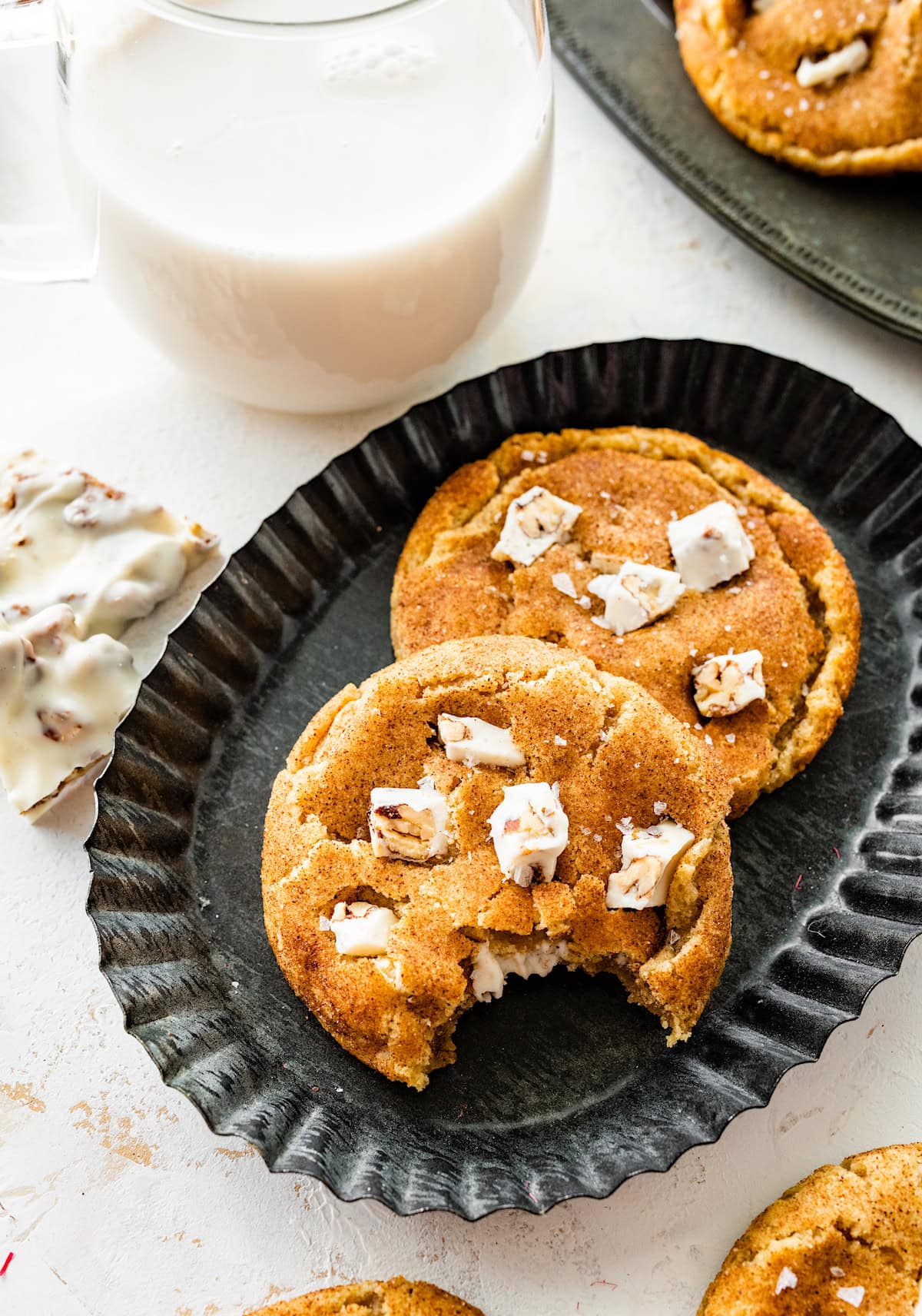 2 Brown Butter White Chocolate Candied Pecan Cookies on plate with one missing a bite.