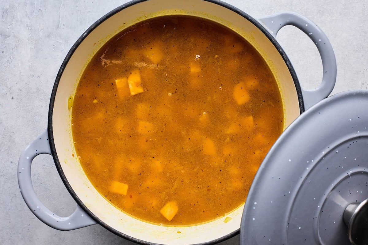 broth added to Creamy Coconut Ginger Sweet Potato Soup in pot. with lid.