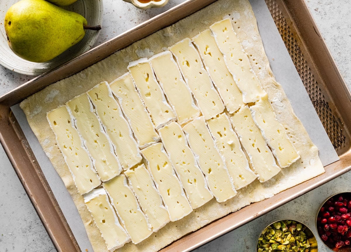 brie slices on sheet of puff pastry on baking sheet.