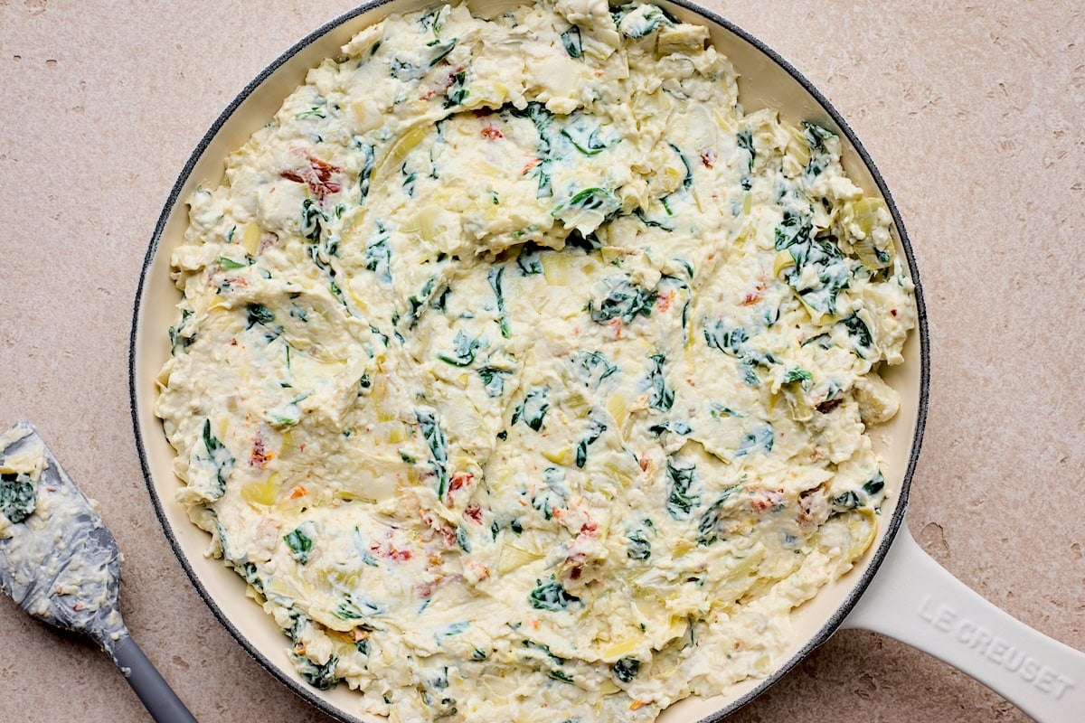 spinach artichoke sun-dried tomato dip spread in cast iron skillet.