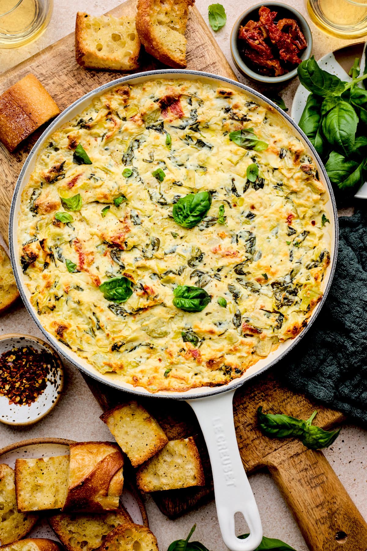 spinach artichoke sun-dried tomato dip in cast iron skillet with bread.