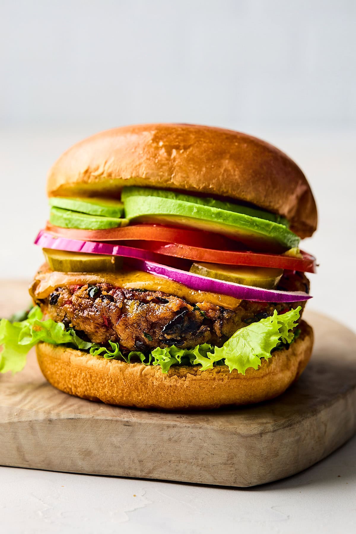 black bean burger on bun with melted cheese, lettuce, red onion, pickles, tomato, and avocado.
