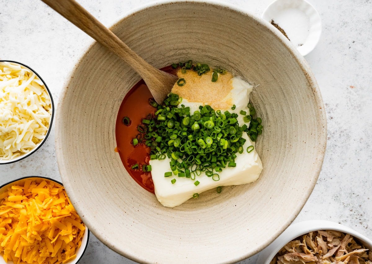 cream cheese, green onions, buffalo sauce, and seasonings in mixing bowl with wooden spoon.