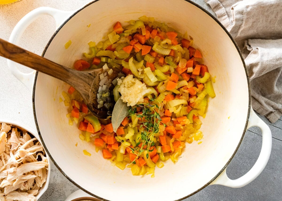 onion, carrot, celery, garlic, thyme cooking in pot with wooden spoon to make chicken and rice.
