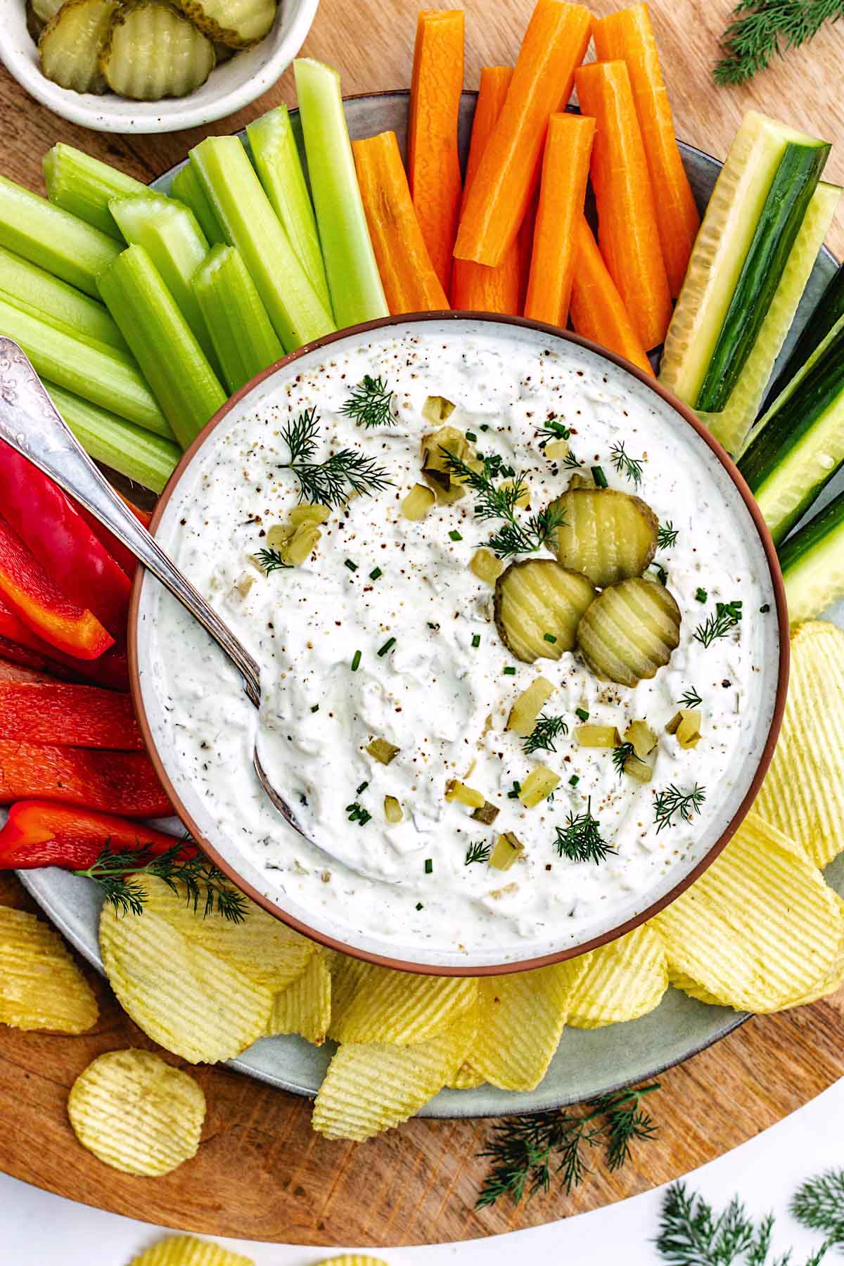dill pickle dip on platter with potato chips and vegetables.