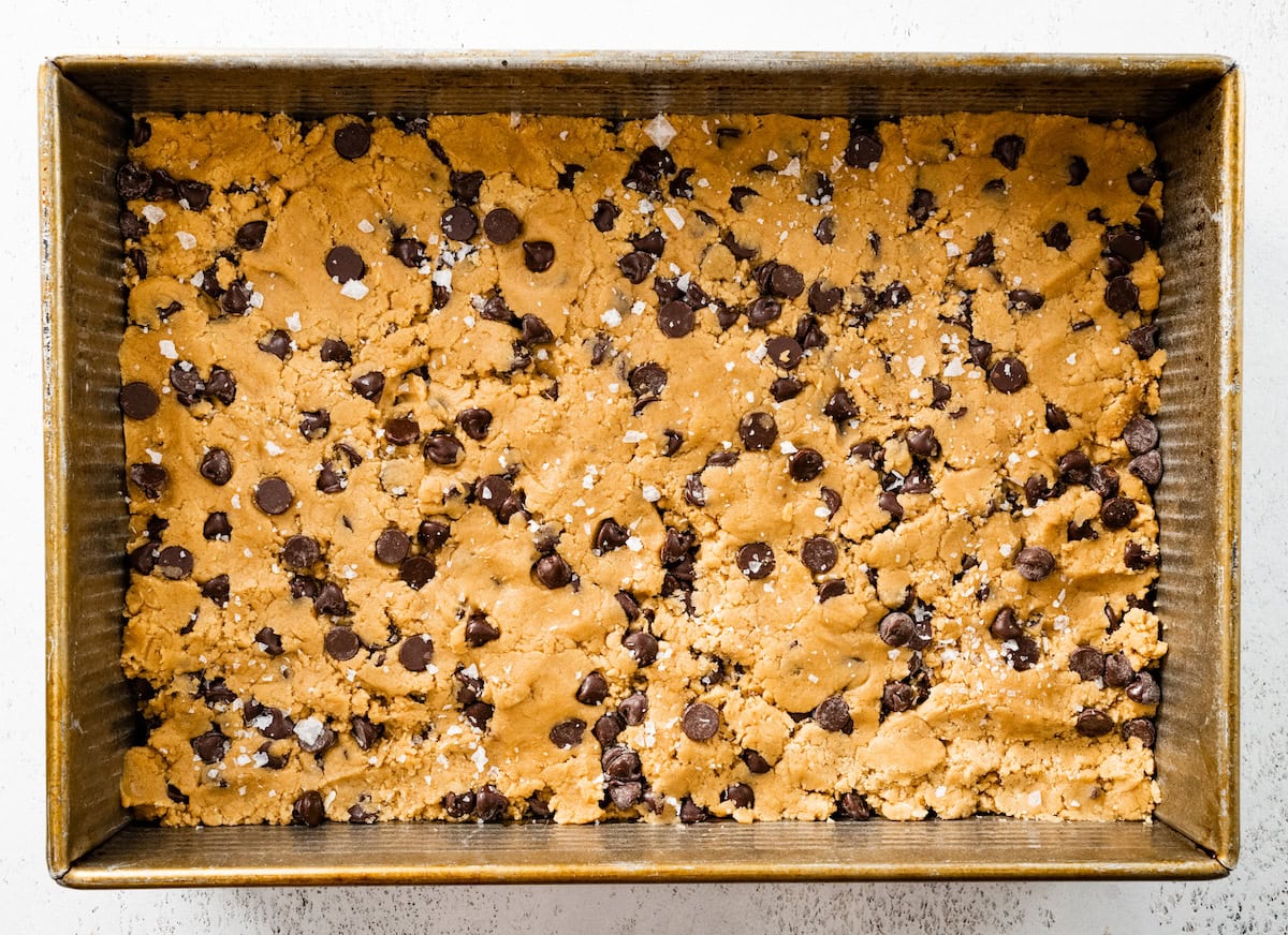 chocolate chip cookie dough pressed into baking pan ready to be baked.