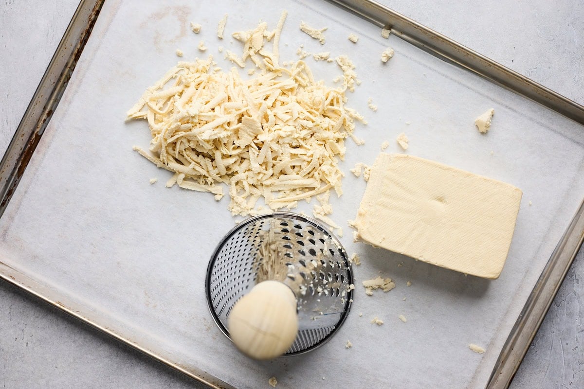 shredding tofu with grater on baking sheet.