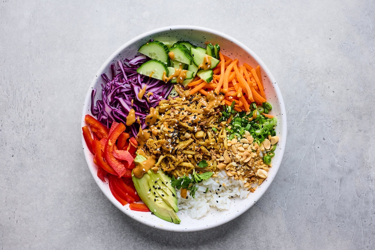 assembled shredded tofu peanut bowls with vegetables, rice, and peanut sauce.