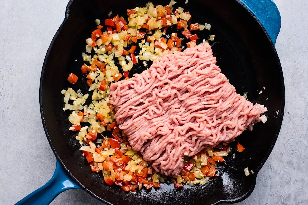 ground turkey cooking in cast iron skillet with onion and red bell peppers.