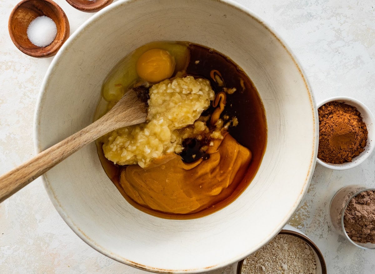 mashed banana, peanut butter, maple syrup, egg, and vanilla in mixing bowl with wooden spoon.