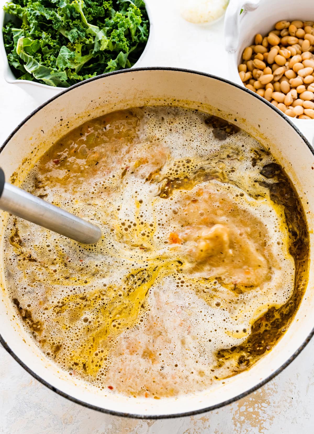 immersion blender blending sausage kale white bean soup in pot.