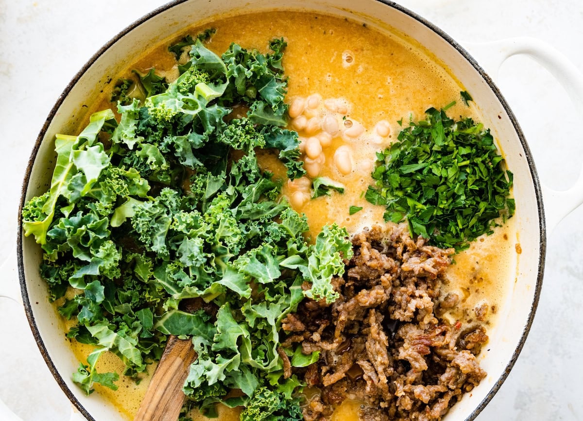 kale, sausage, and parsley being added to soup.