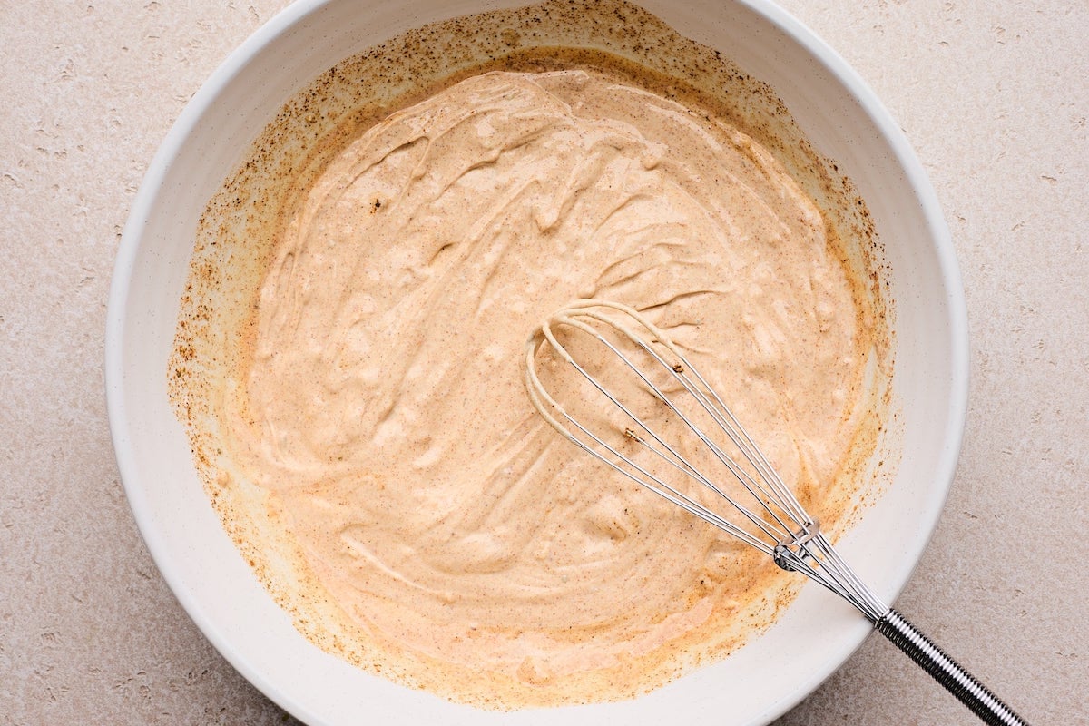 creamy Greek yogurt dressing with taco seasoning in bowl with whisk.