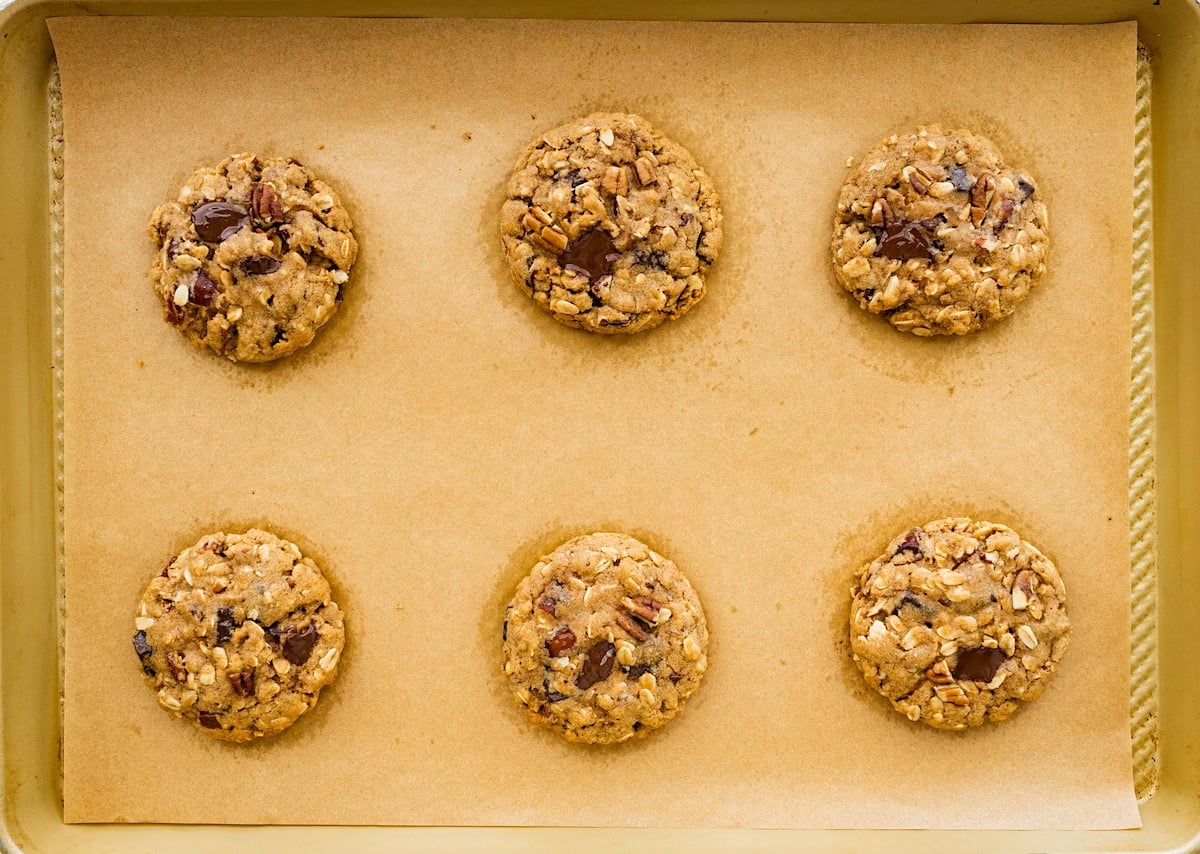 brown butter oatmeal cookies with pecans, dates, and chocolate chunks on baking sheet with parchment paper.