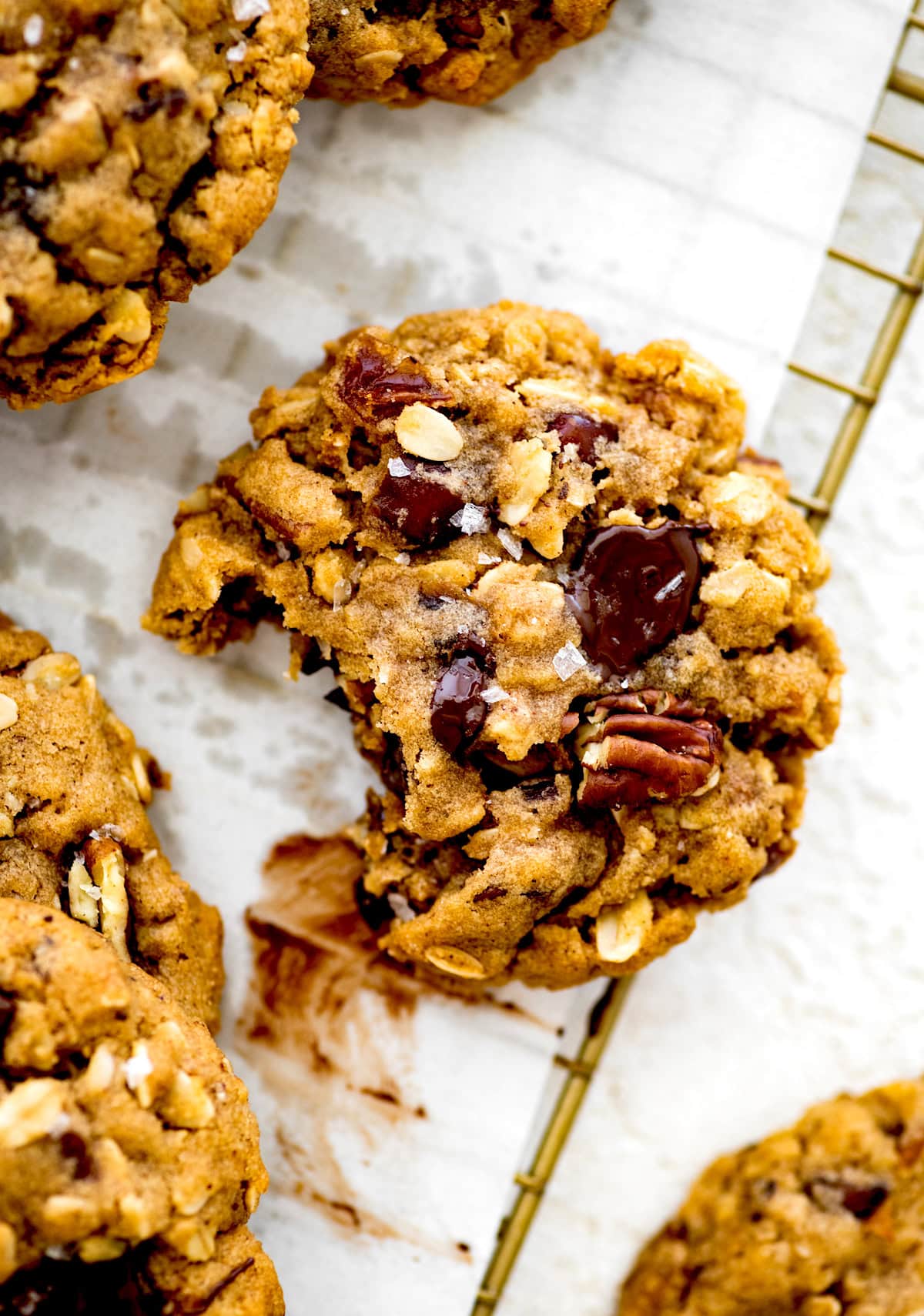 brown butter oatmeal cookie with pecans, dates, and chocolate chunks on cooling rack with bite taken out of the cookie.