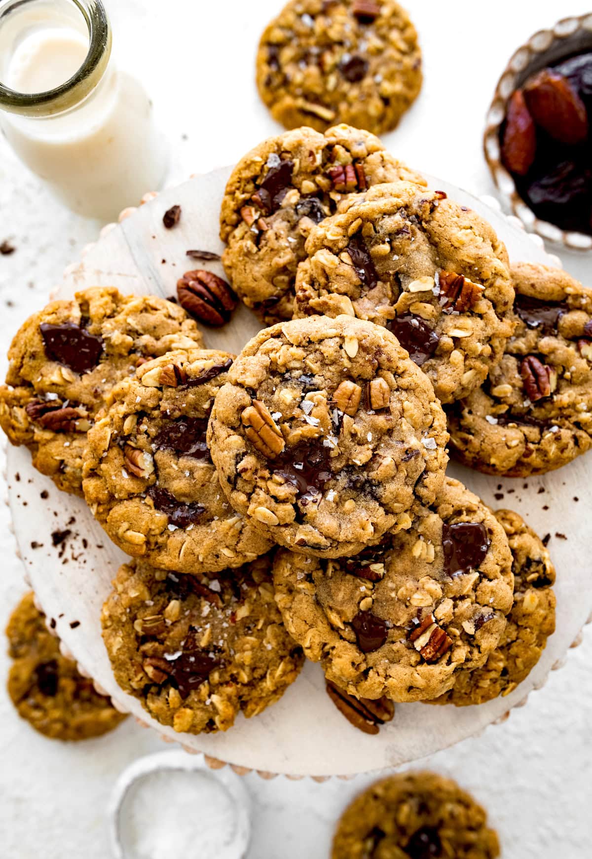 brown butter oatmeal cookies with pecans, dates, and chocolate chunks on plate with bottle of milk.