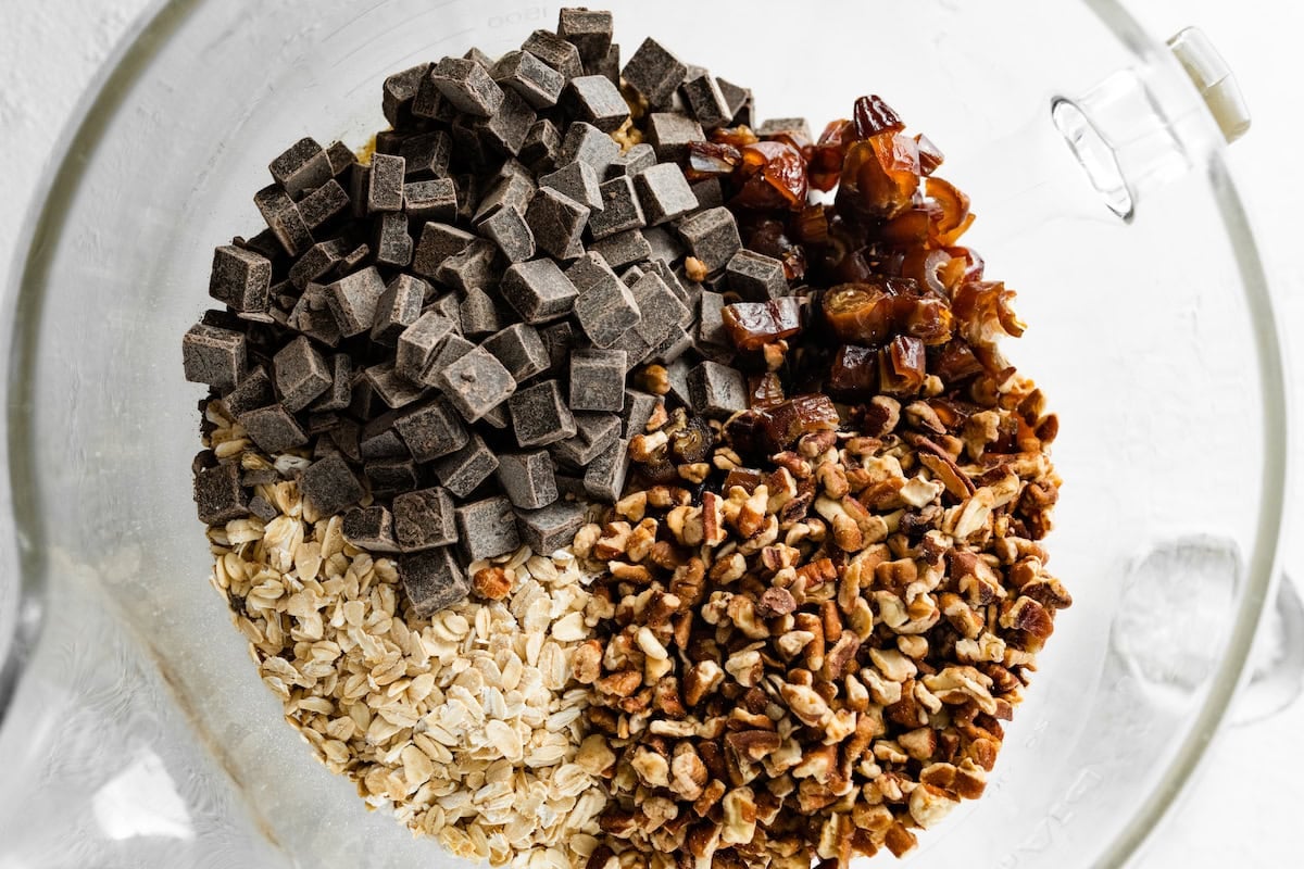 chopped pecans, dates, and chocolate chunks being added to oatmeal cookie dough.