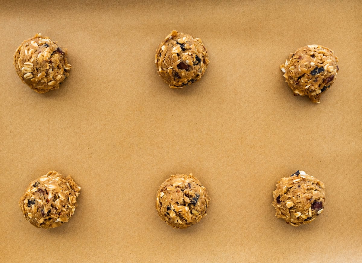 brown butter oatmeal cookie dough balls with pecans, dates, and chocolate chunks on baking sheet with parchment paper.