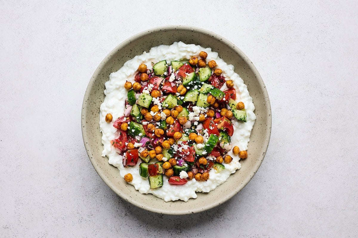 cottage cheese salad in bowl with crispy chickpeas, tomato, cucumber, red onion, and feta on top.