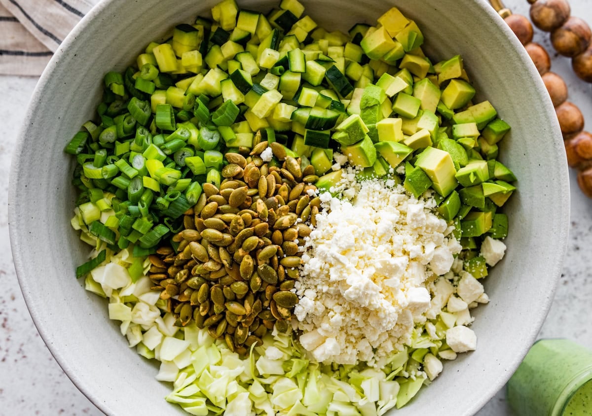 cabbage, green onion, cucumber, avocado, pepitas, and feta cheese in big bowl to make green goddess salad.